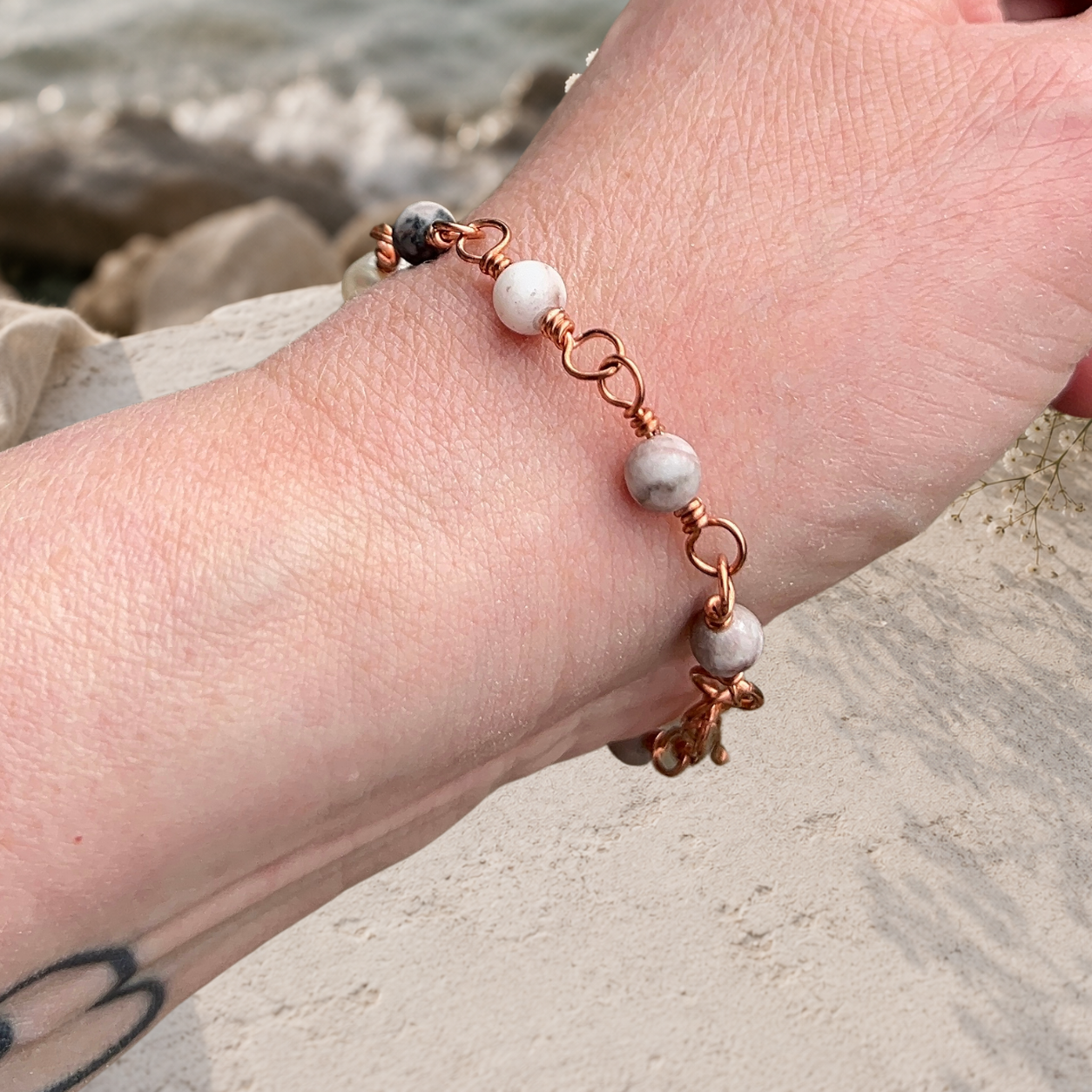 Närbild på handgjort koppararmband med jaspis och omsmyckad sötvattenpärla i koppartråd